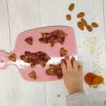 Rosafarbenes Brettchen auf dem Kekse in Schweinchenform liegen, Kinderhand ist im Bild